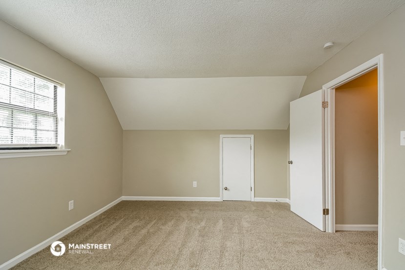 the spacious living room with carpeted flooring and an open door to the bedroom
