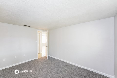 the living room of an apartment with carpet and white walls