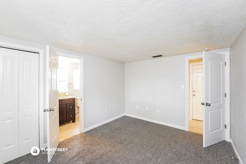 a bedroom with white walls and carpet and a door to a bathroom