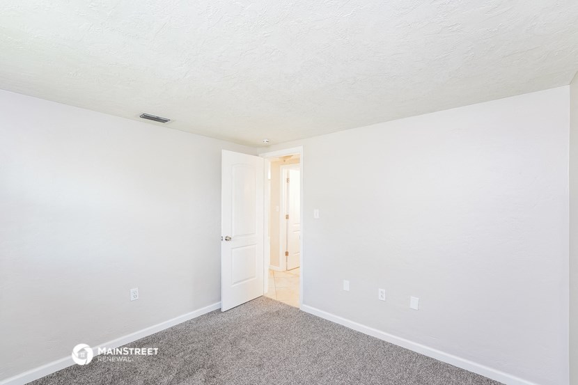a bedroom with white walls and carpet and a door to a hallway