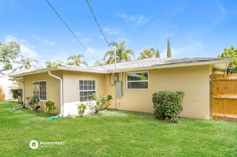 a small beige house with a lawn and a wooden fence