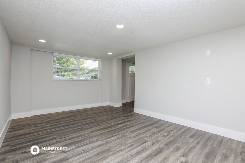 the living room of an apartment with wood flooring and a window