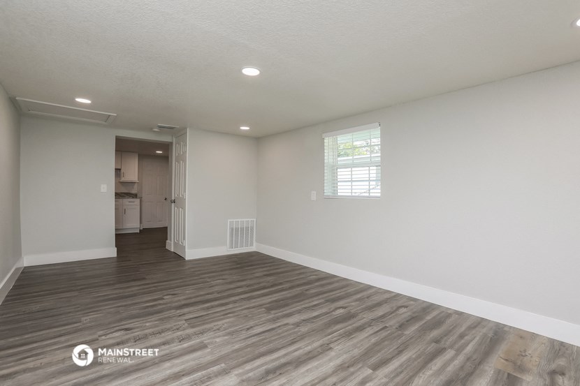 the living room of an apartment with white walls and wood flooring