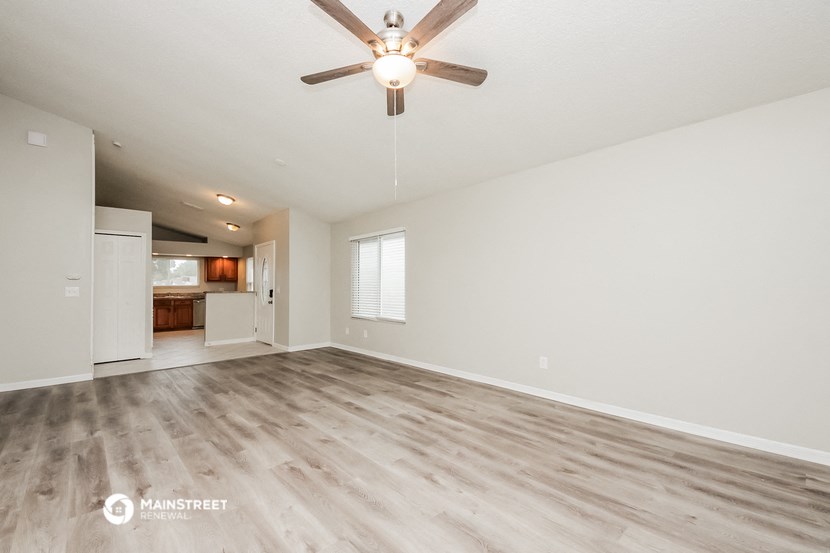 an empty living room with a ceiling fan and a kitchen