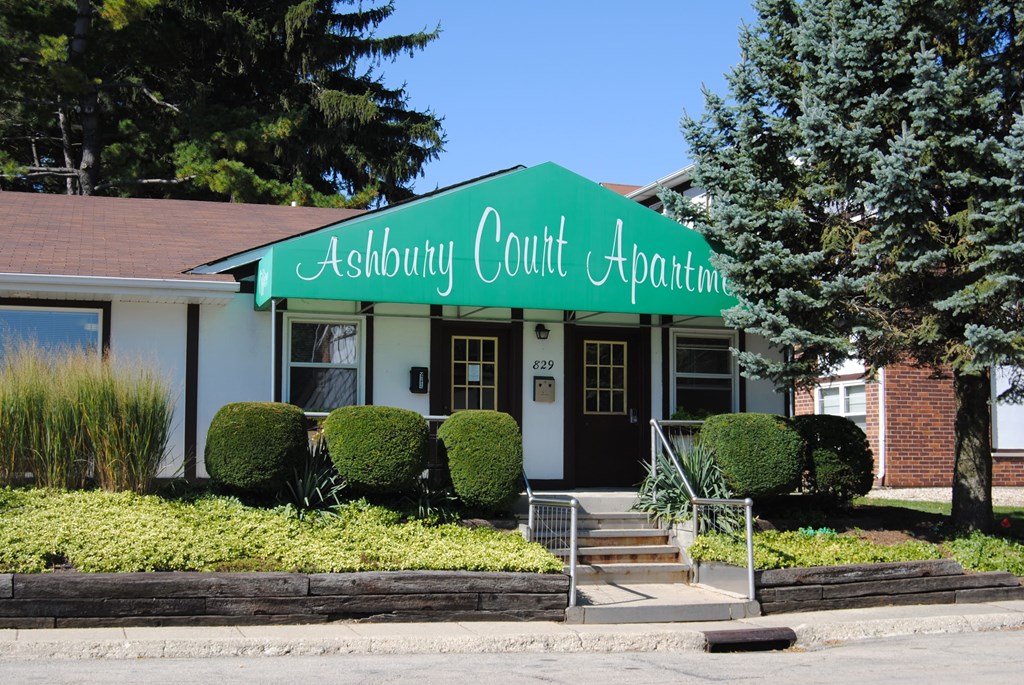 A white building with a green awning that says Ashbury Court Apartment.
