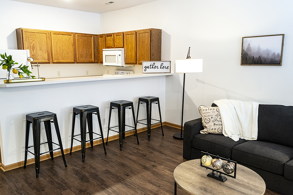 a living room with a bar and a kitchen with stools