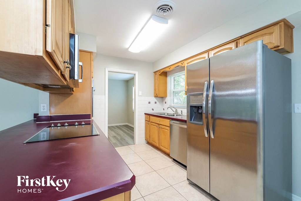 A kitchen with a refrigerator, wooden cabinets, and a maroon countertop.