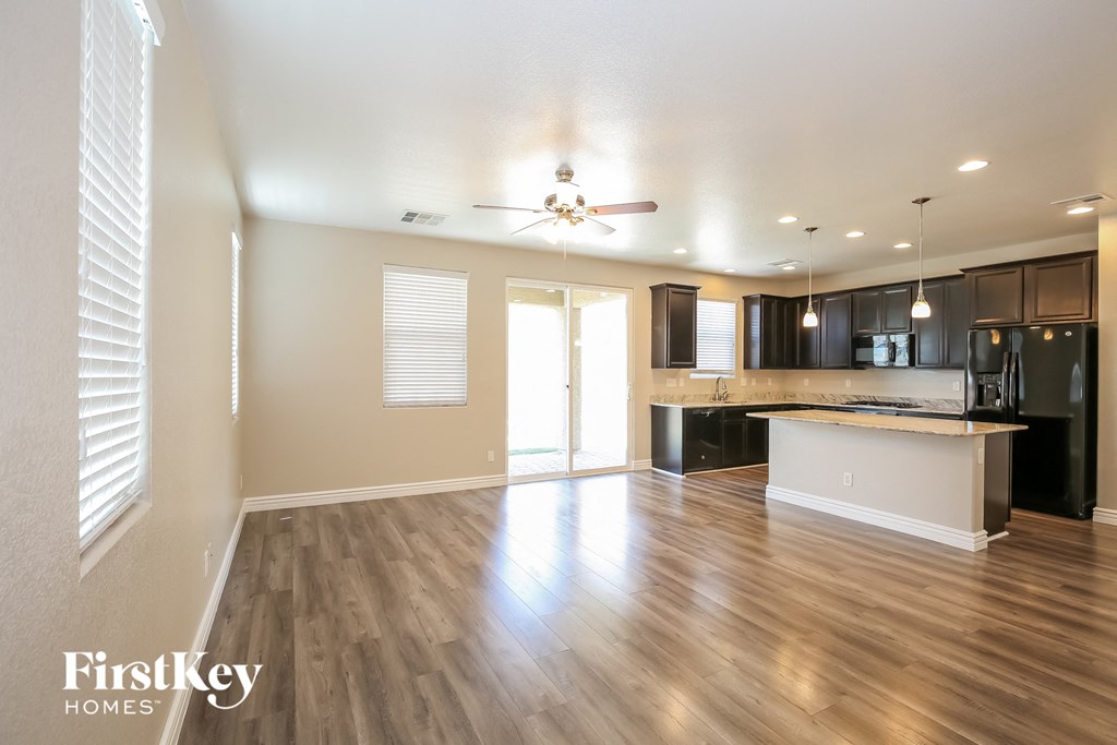 an empty living room with a kitchen and a ceiling fan