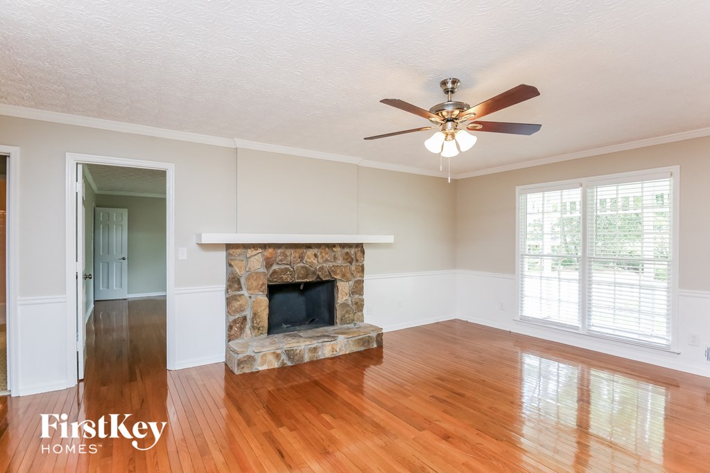 an empty living room with a stone fireplace and a ceiling fan