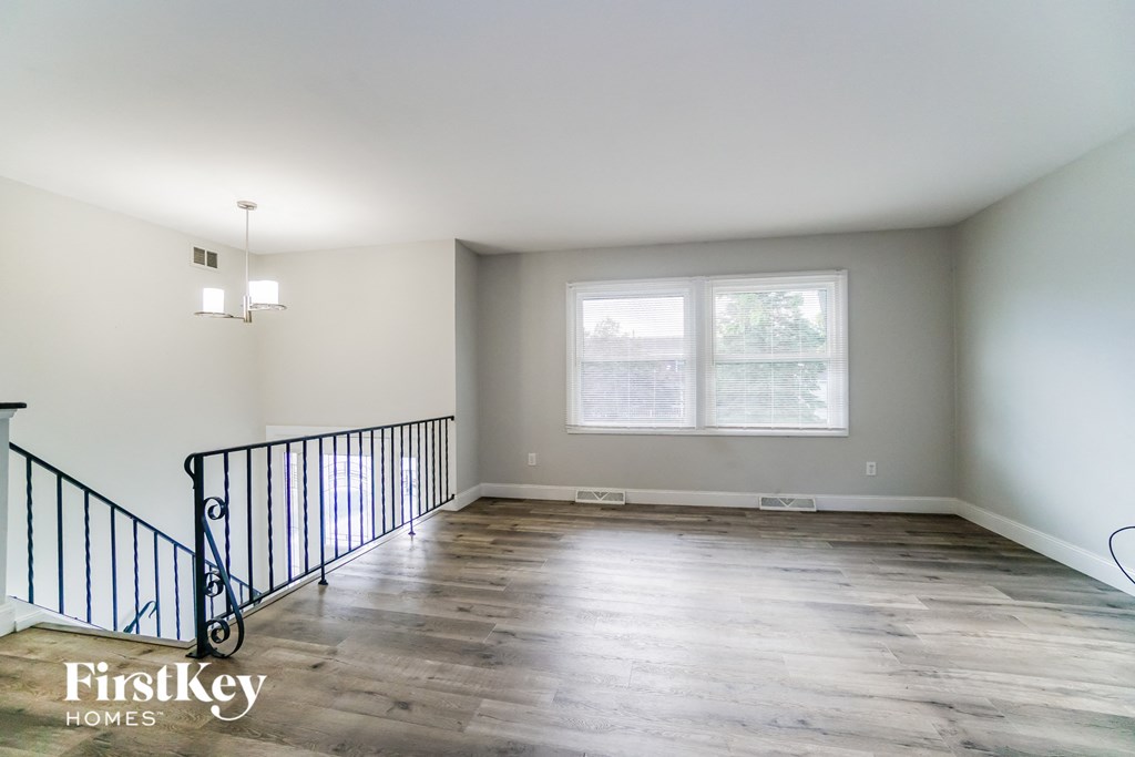 A spacious room with a wooden floor and a staircase with a black railing.
