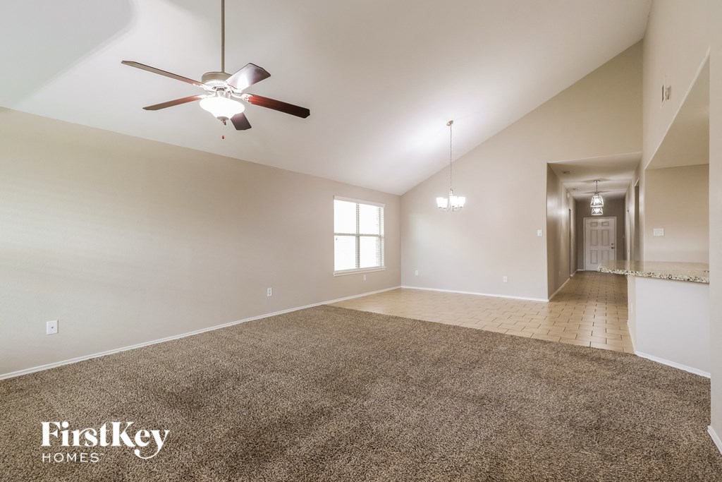a spacious living room with carpet and a ceiling fan