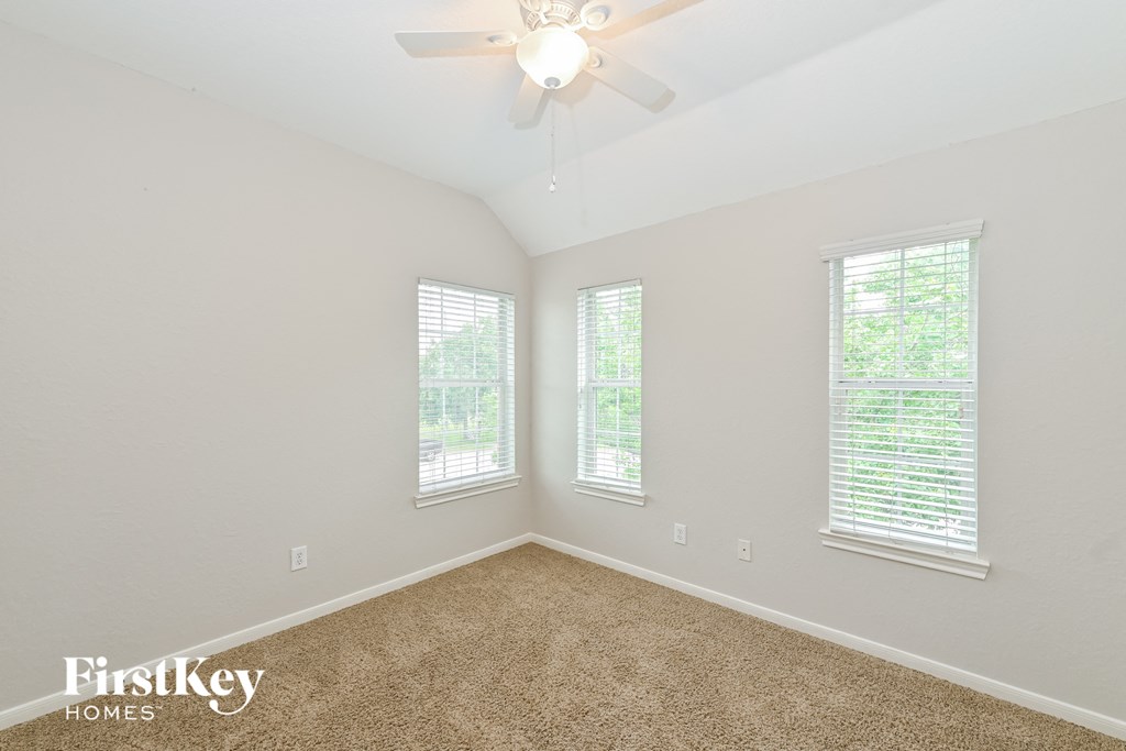the spacious living room with three windows and a ceiling fan