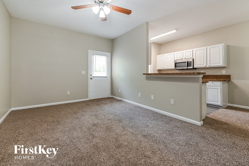 an empty living room with a kitchen and a ceiling fan