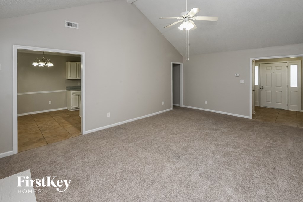 an empty living room with a ceiling fan and a door to a kitchen