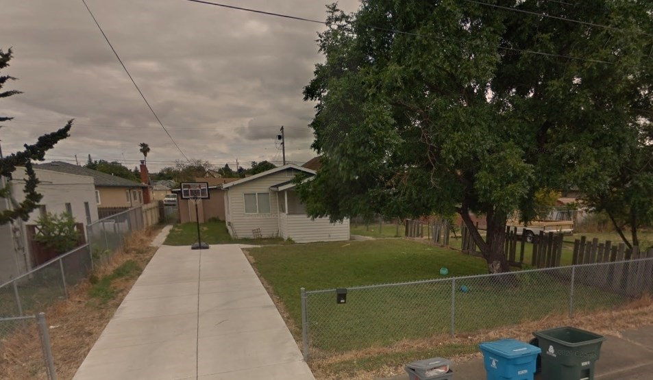 A residential street with a sidewalk, houses, and trees.