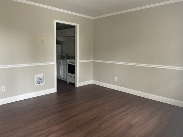 an empty living room with a wooden floor and a door to a kitchen