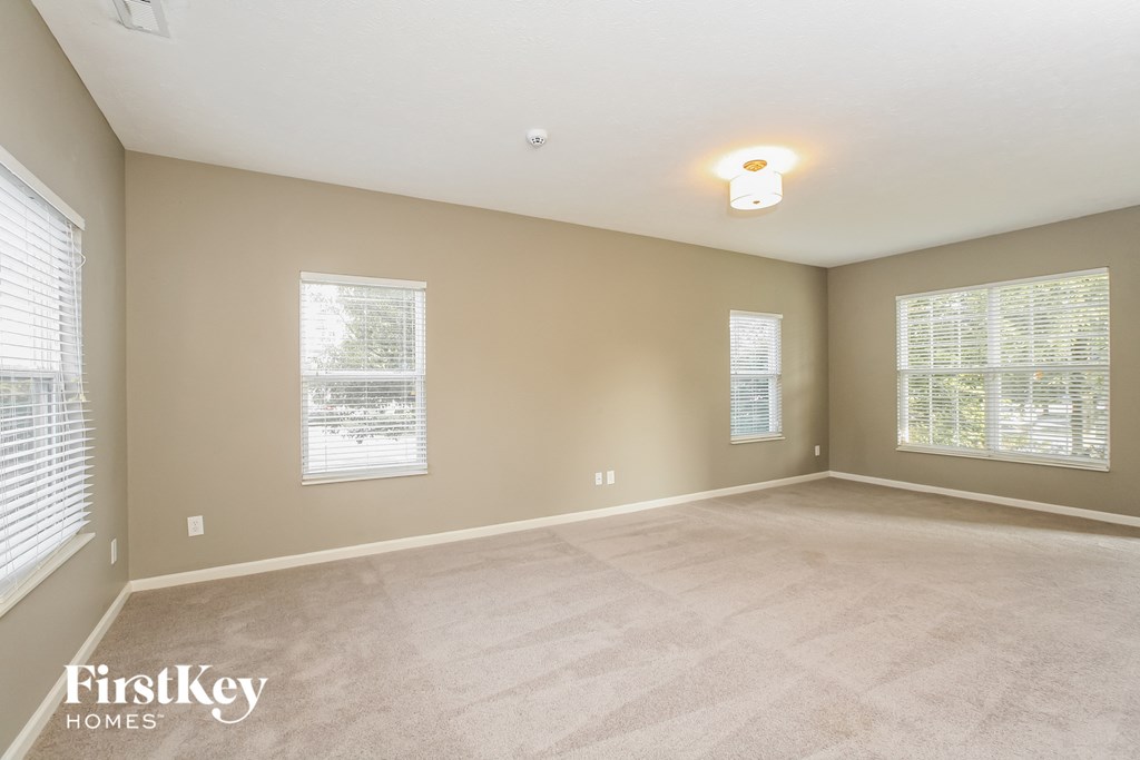 an empty living room with three windows and a carpeted floor