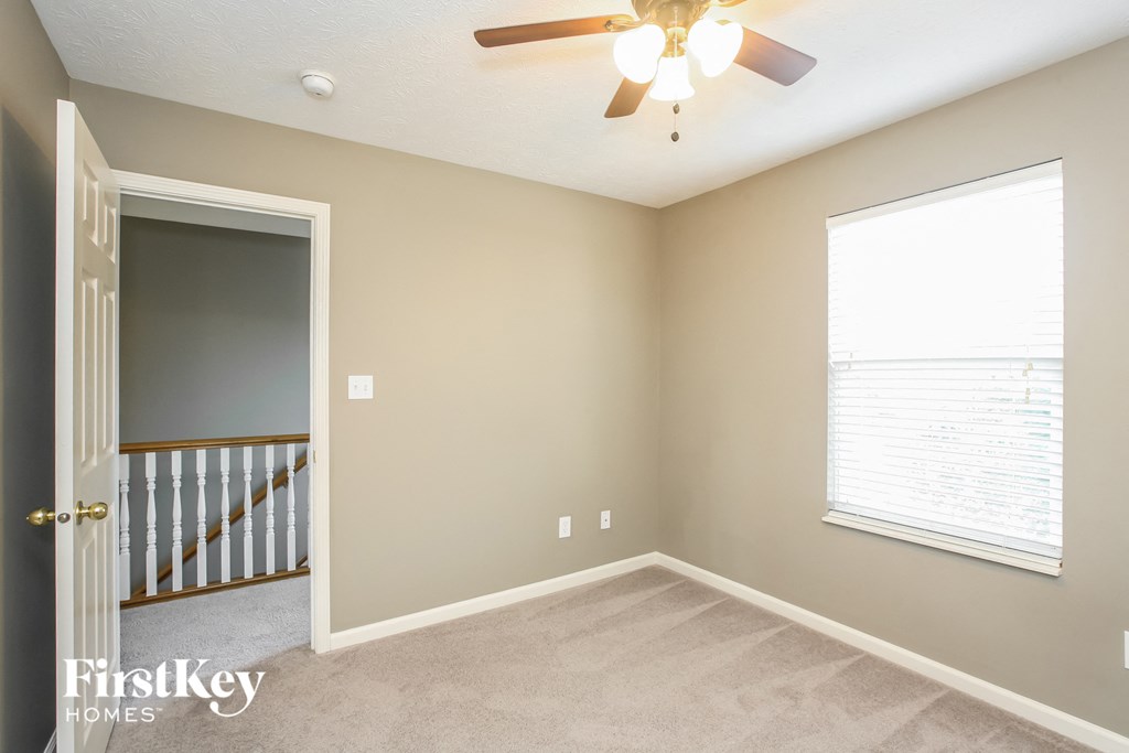 an empty bedroom with a ceiling fan and a door to a staircase