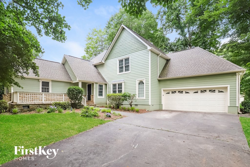 A two-story house with a garage is surrounded by greenery.