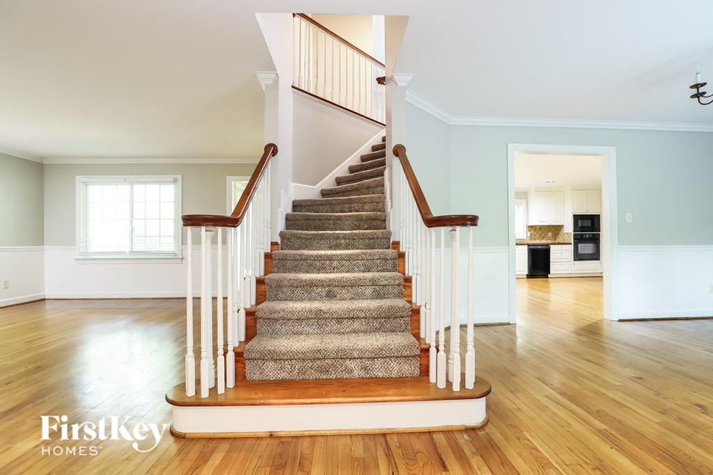 A staircase with a wooden handrail and a carpeted runner leads up to a landing with a doorway.