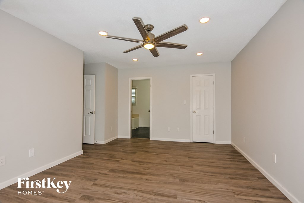 a empty living room with a ceiling fan and a door to a bathroom