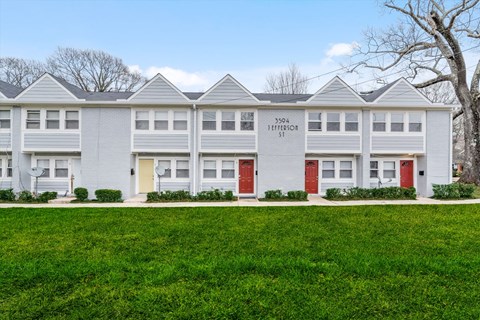 a white apartment building with red doors and a lawn