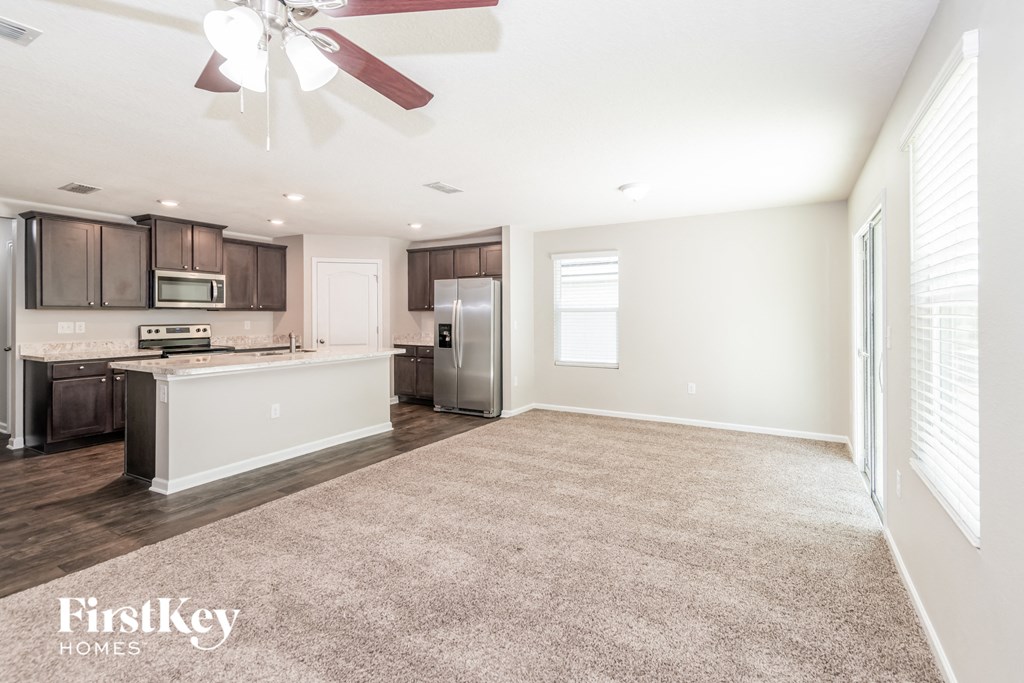 an empty living room with a kitchen and a ceiling fan