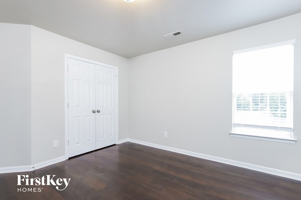 a bedroom with white walls and wood floors and a window