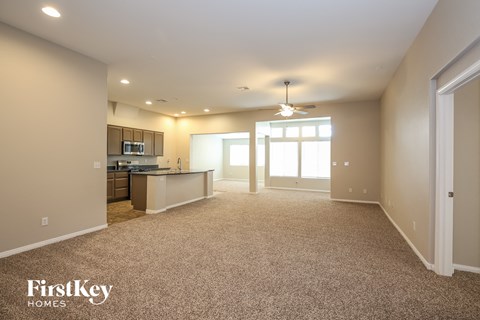 A spacious living room with a kitchen in the background and a carpeted floor.