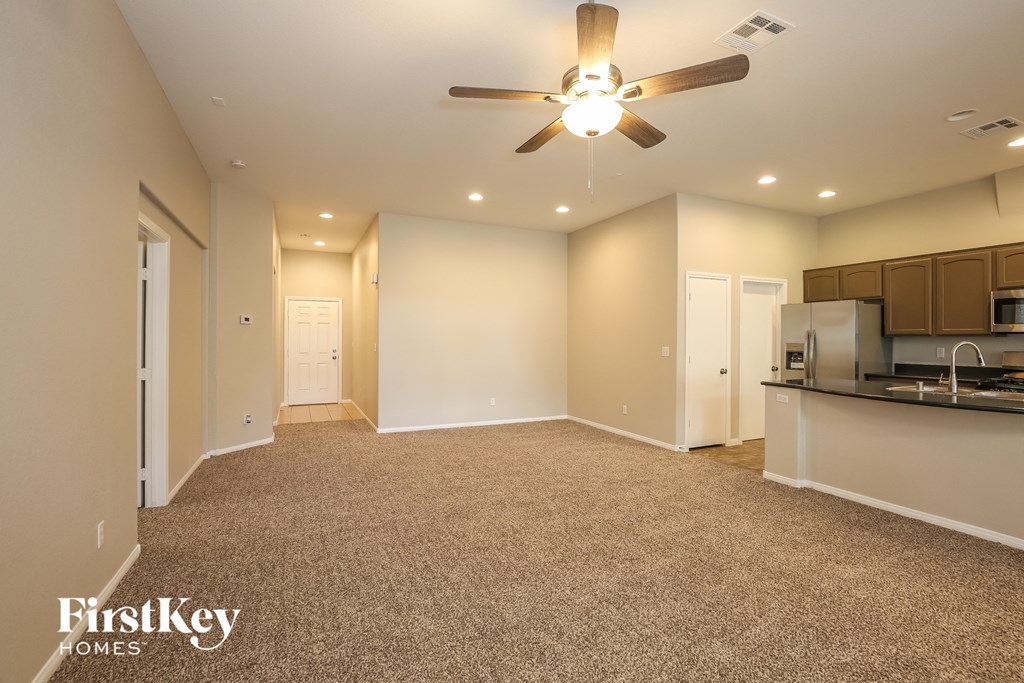 A spacious room with a ceiling fan and a kitchen area in the background.