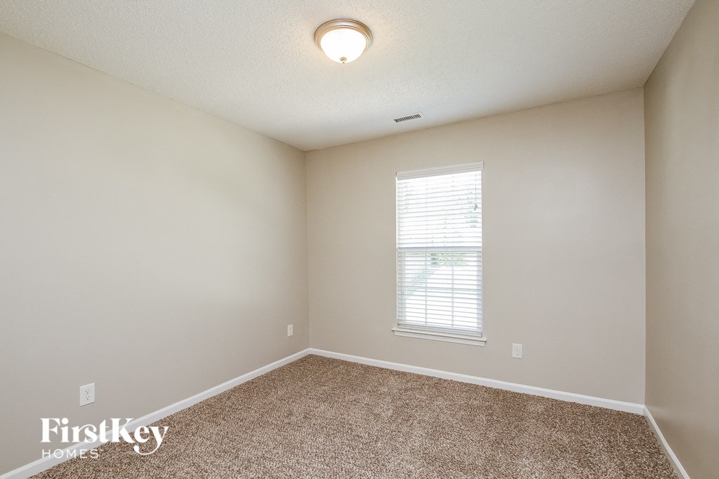 A room with a carpet floor and a window with blinds.