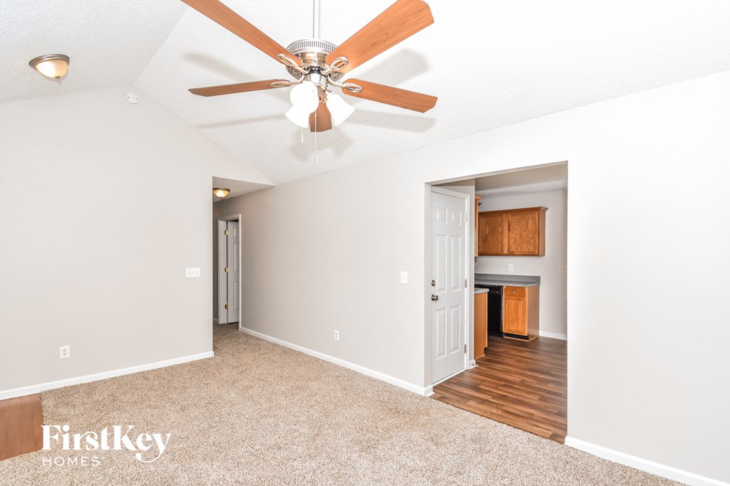 a living room with a ceiling fan and a door to a kitchen