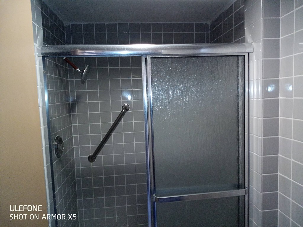 a shower in a white tiled bathroom with a glass door