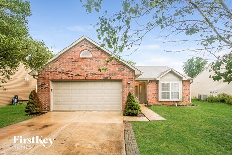 A brick house with a garage door and a small tree in front of it.