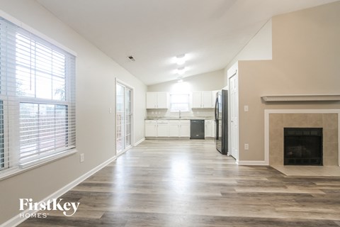A spacious living room with a fireplace and a kitchen in the background.