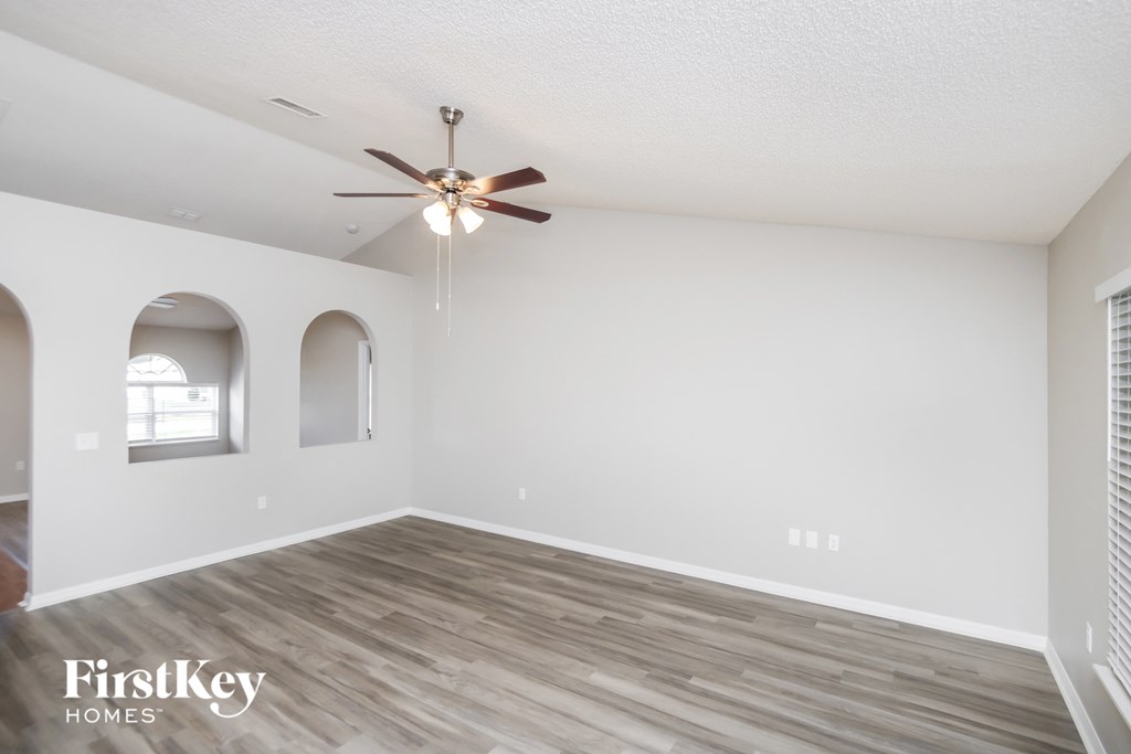 the spacious living room with hardwood flooring and a ceiling fan