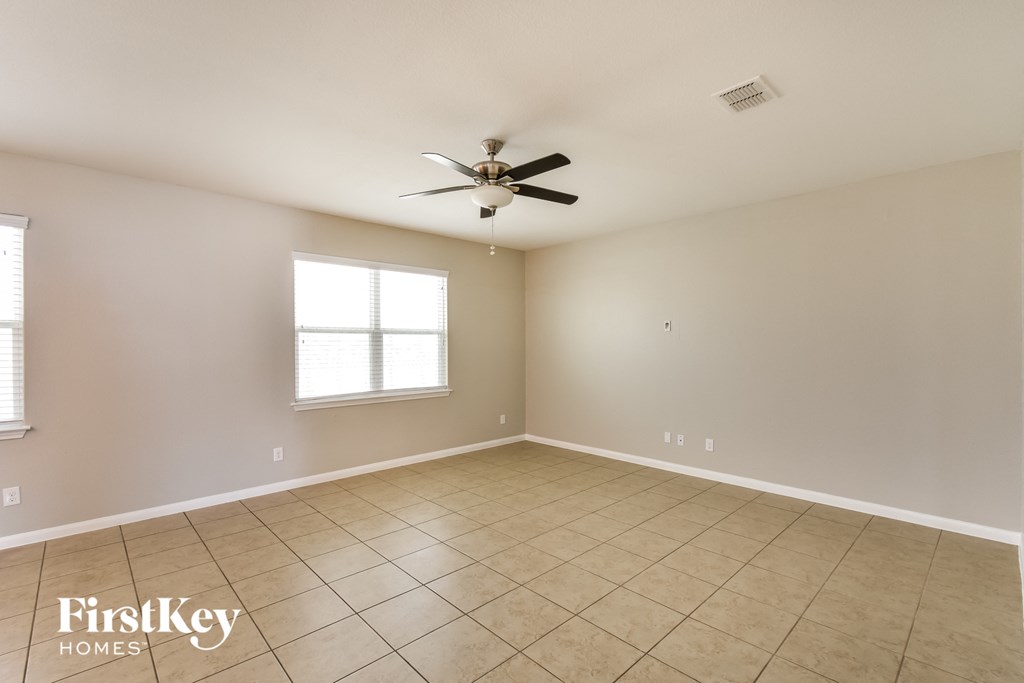 an empty living room with a ceiling fan and tiled floors