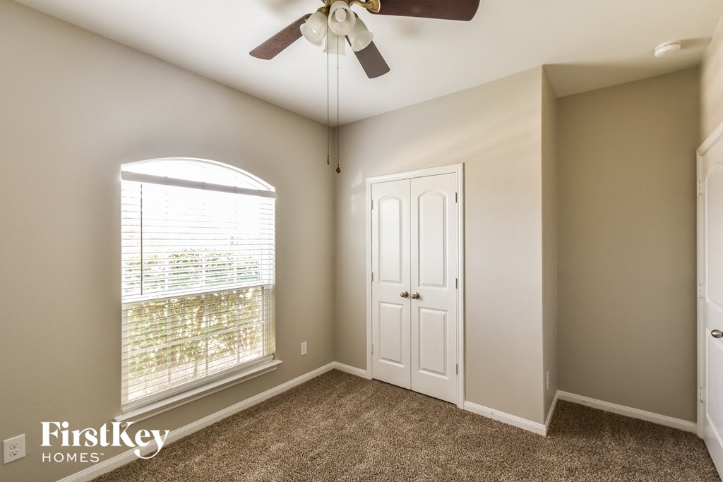 an empty bedroom with a ceiling fan and a window
