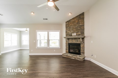 A spacious living room with a stone fireplace and a ceiling fan.