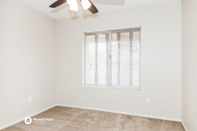 the spacious living room with a large window and a ceiling fan