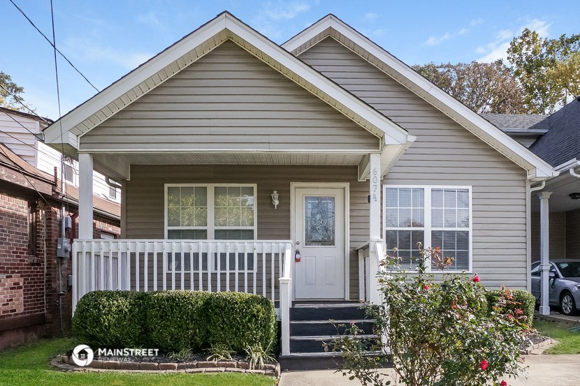 a gray house with a white porch and a white fence