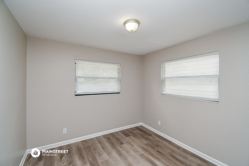 the interior of an empty room with wood flooring and two windows