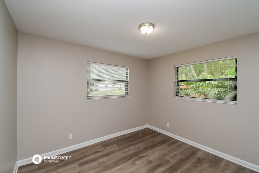 the interior of an empty room with wood flooring and two windows