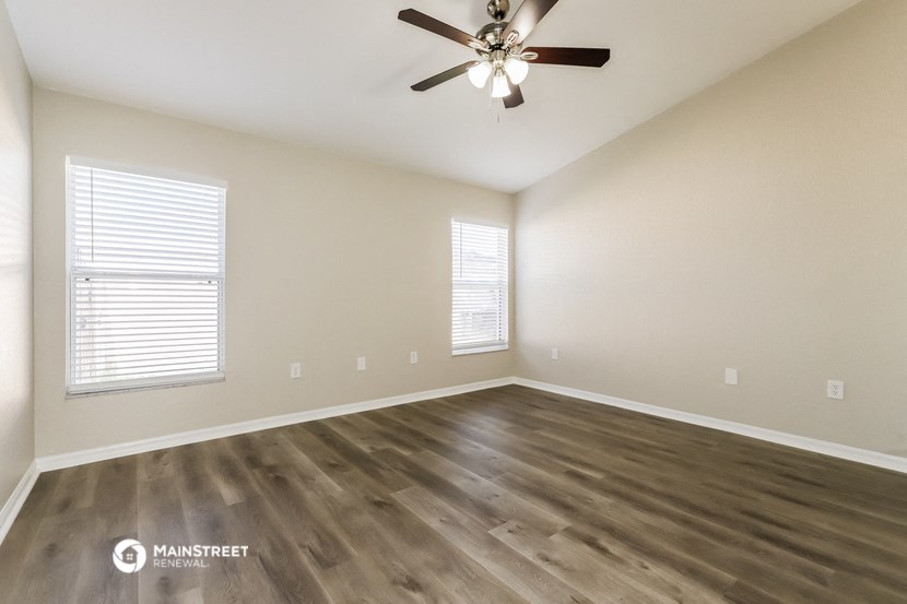 the spacious living room with hardwood floors and a ceiling fan