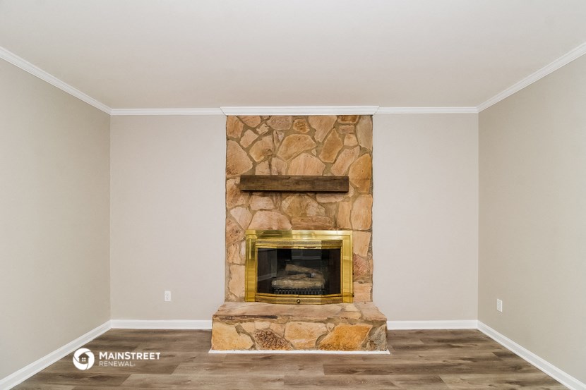 the living room has a stone fireplace and wooden floors