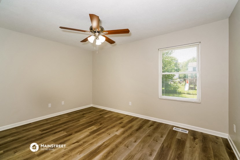 the spacious living room with wood flooring and a ceiling fan