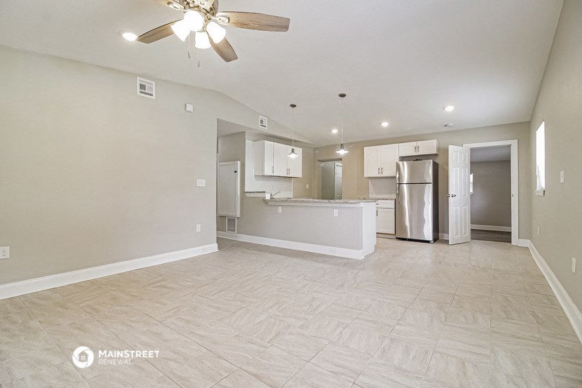 an empty living room with a kitchen and a ceiling fan