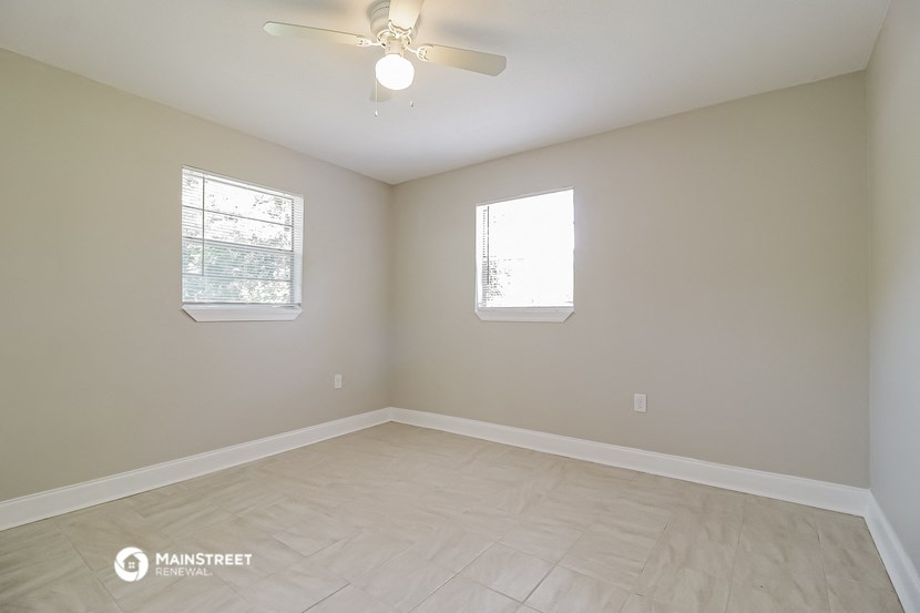 an empty room with a ceiling fan and two windows