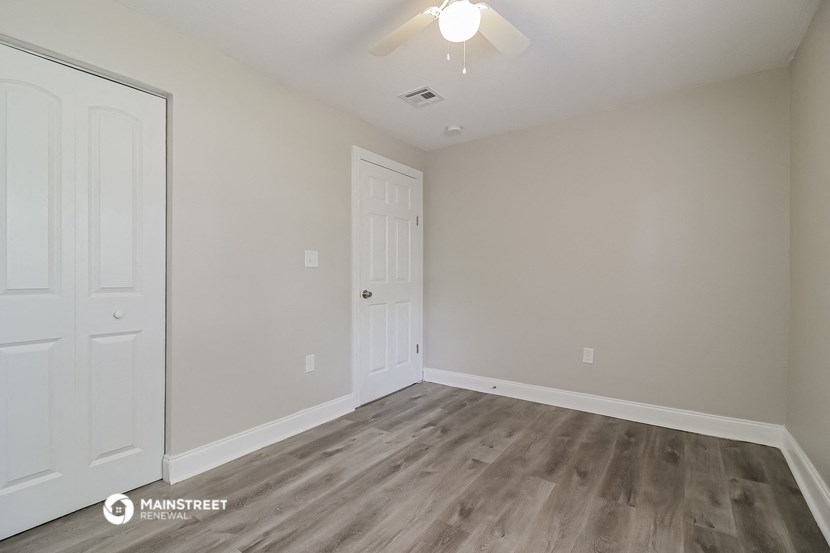 a bedroom with white walls and wood flooring and a closet