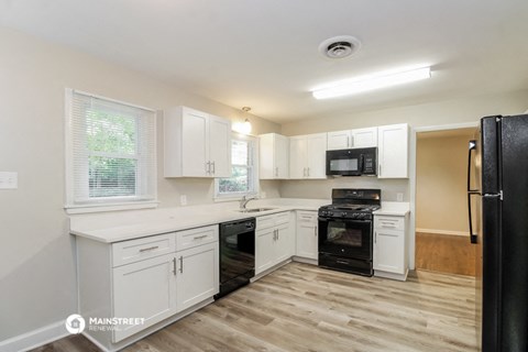 a kitchen with white cabinets and black appliances and a wooden floor
